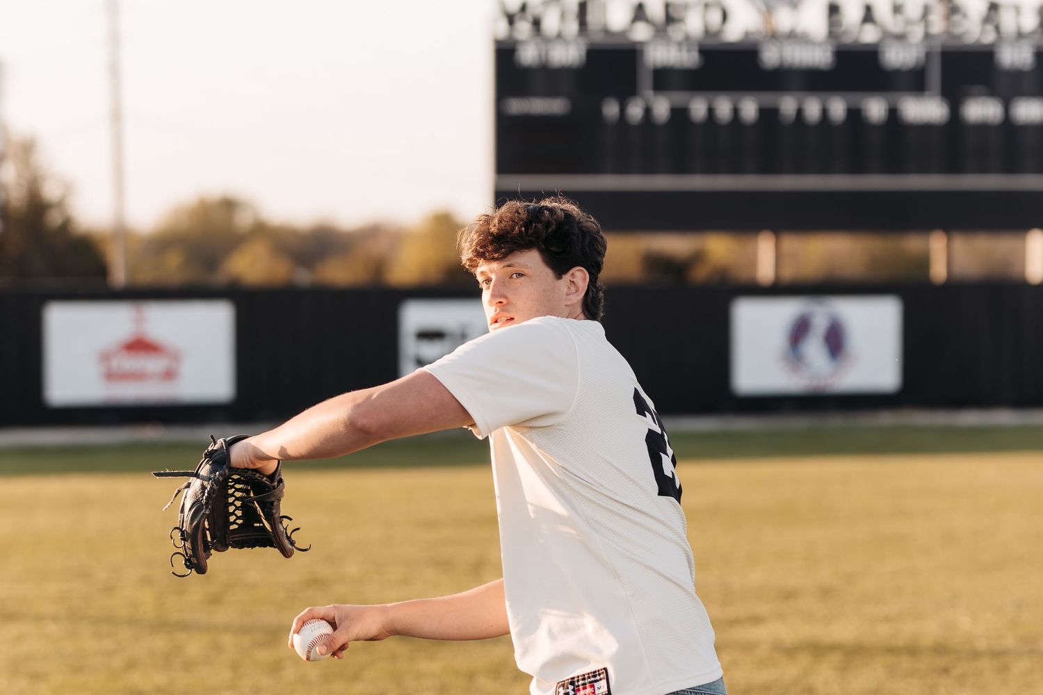 Baseball player in white uniform demonstrating pitching form on field.