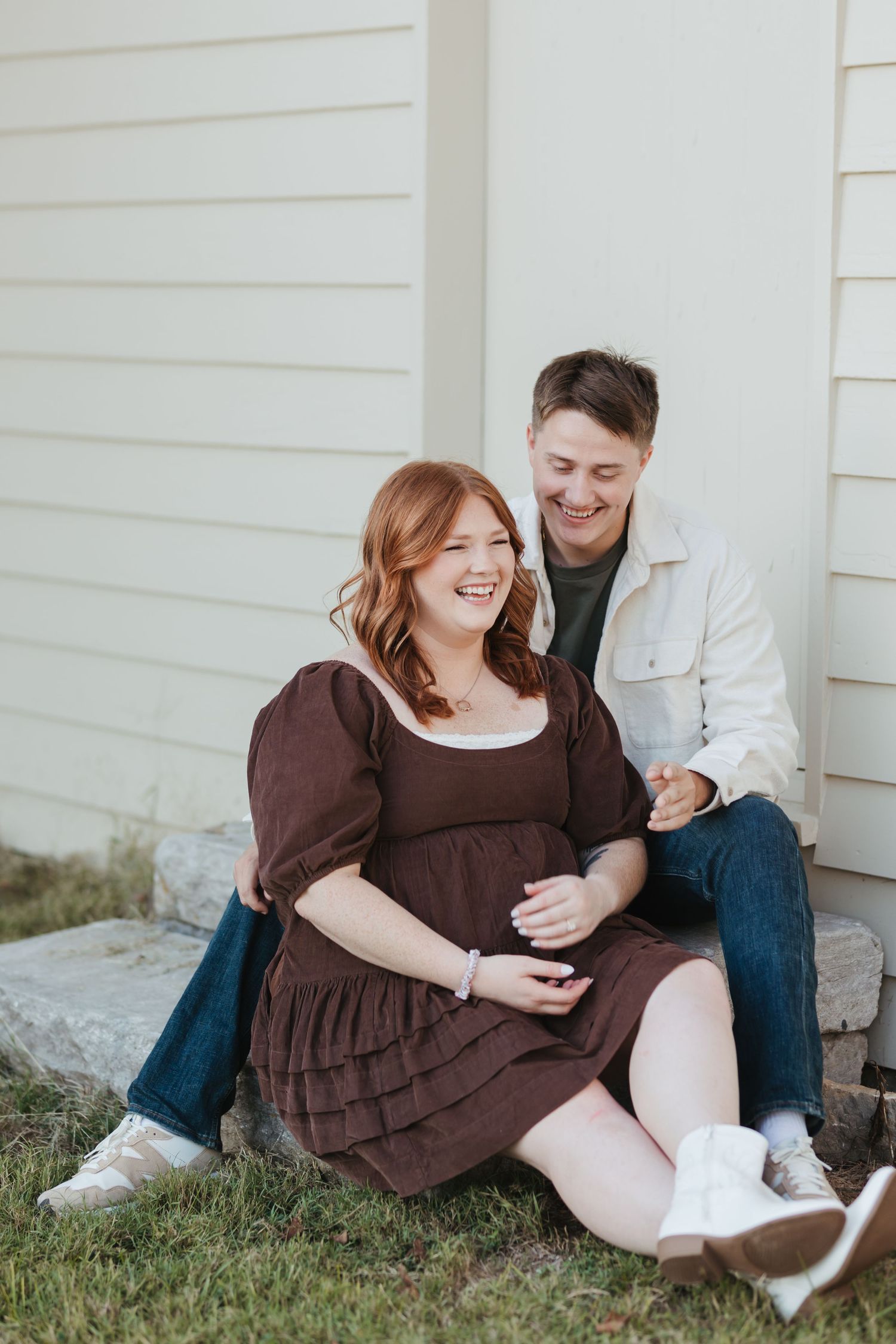 Couple sitting together on stone steps by white siding house sharing joyful laughter.