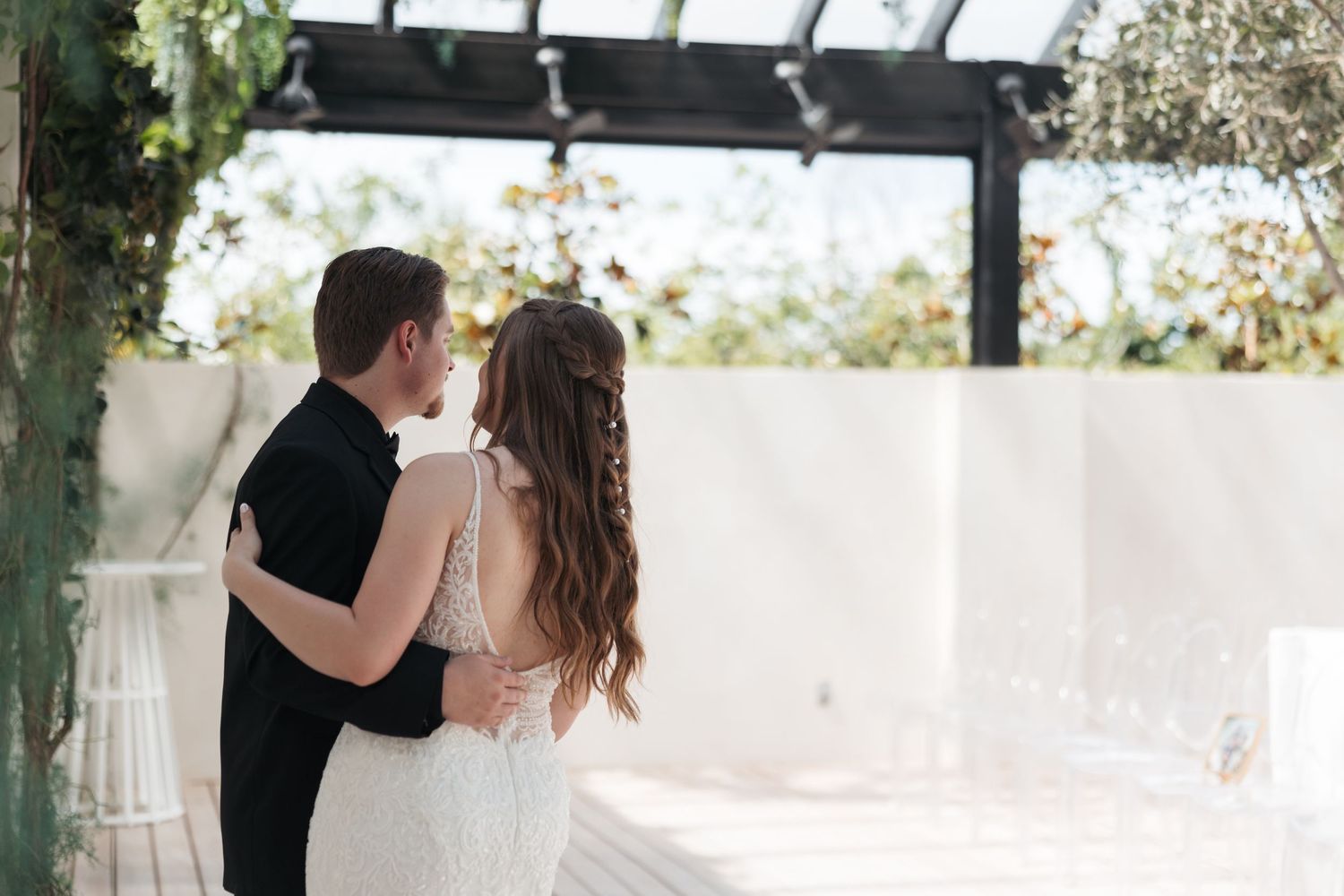 Intimate wedding moment captured under pergola with white walls and greenery.
