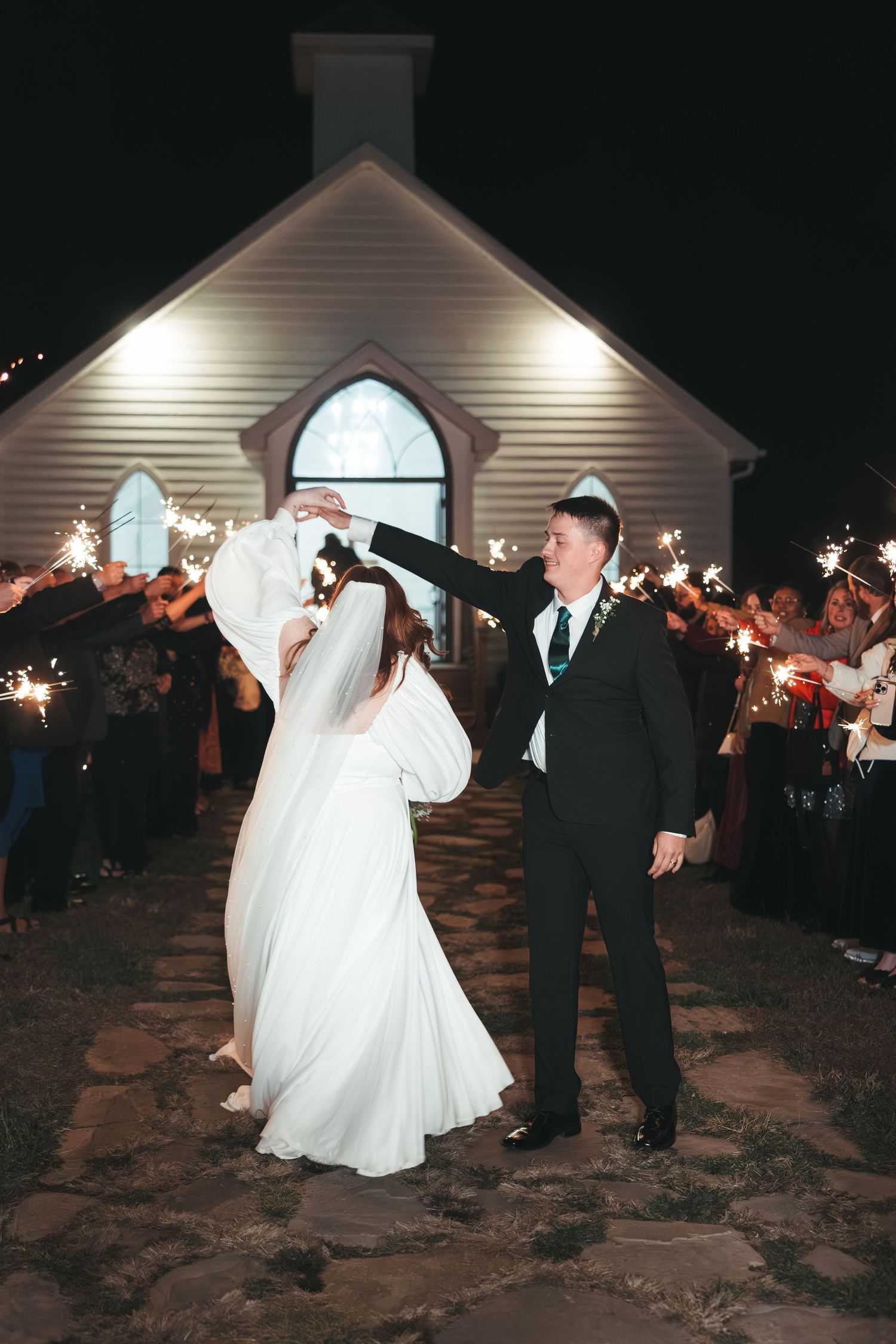 Wedding couple dancing outside illuminated chapel with sparklers.