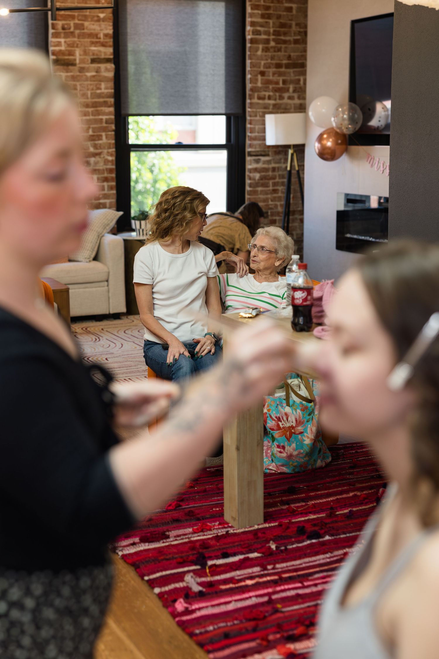Women gathered in a cozy brick-walled living room decorated with balloons for a casual celebration party.