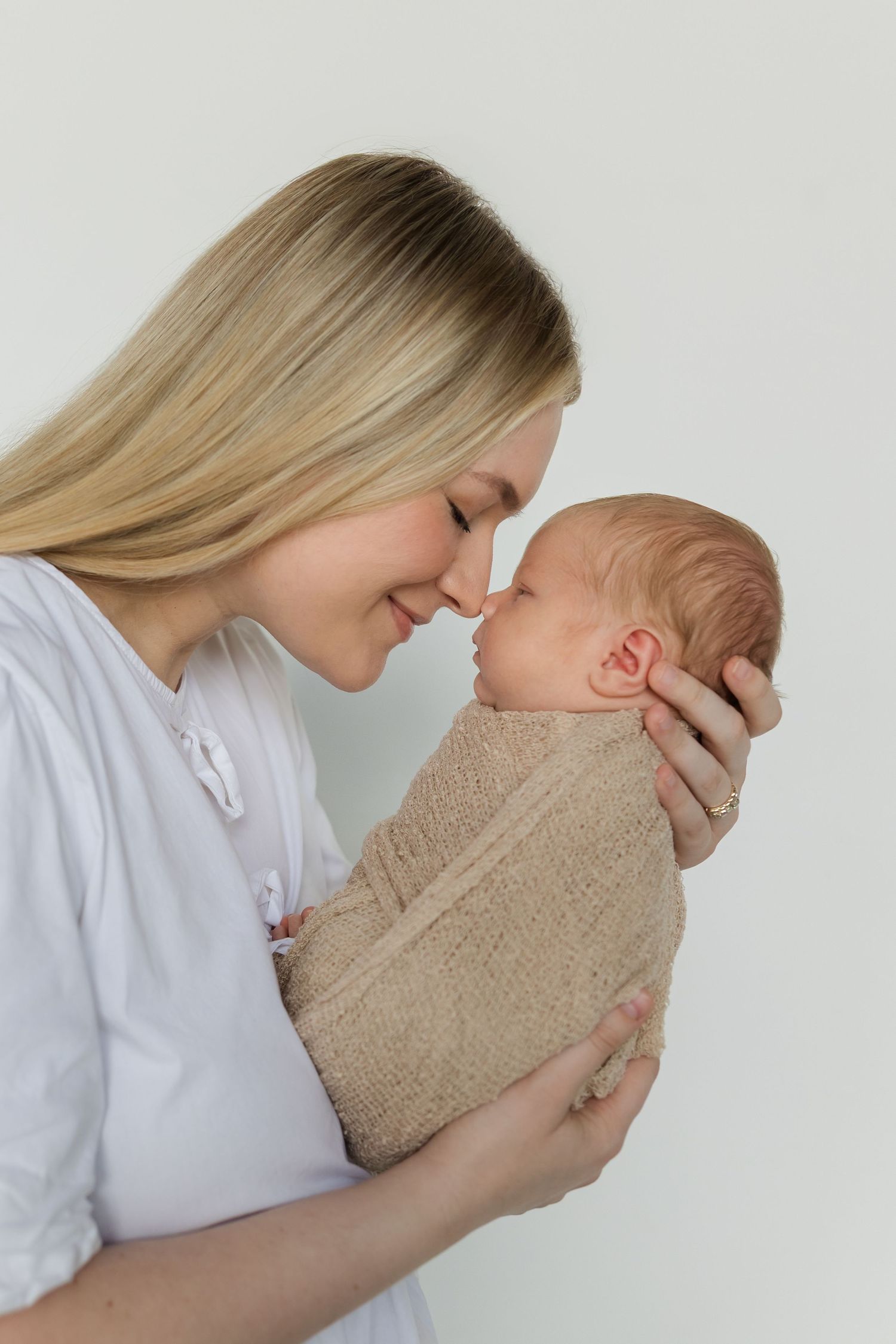A series of tender moments showing a parent cradling and bonding with a newborn baby wrapped in beige knit blanket.