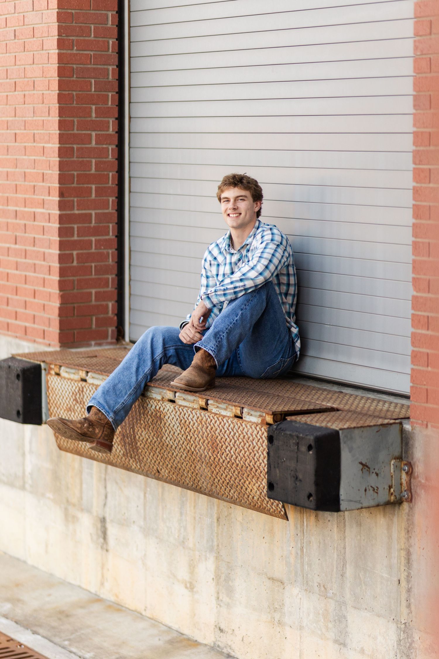Person in plaid shirt relaxes on loading dock ledge against industrial garage door.