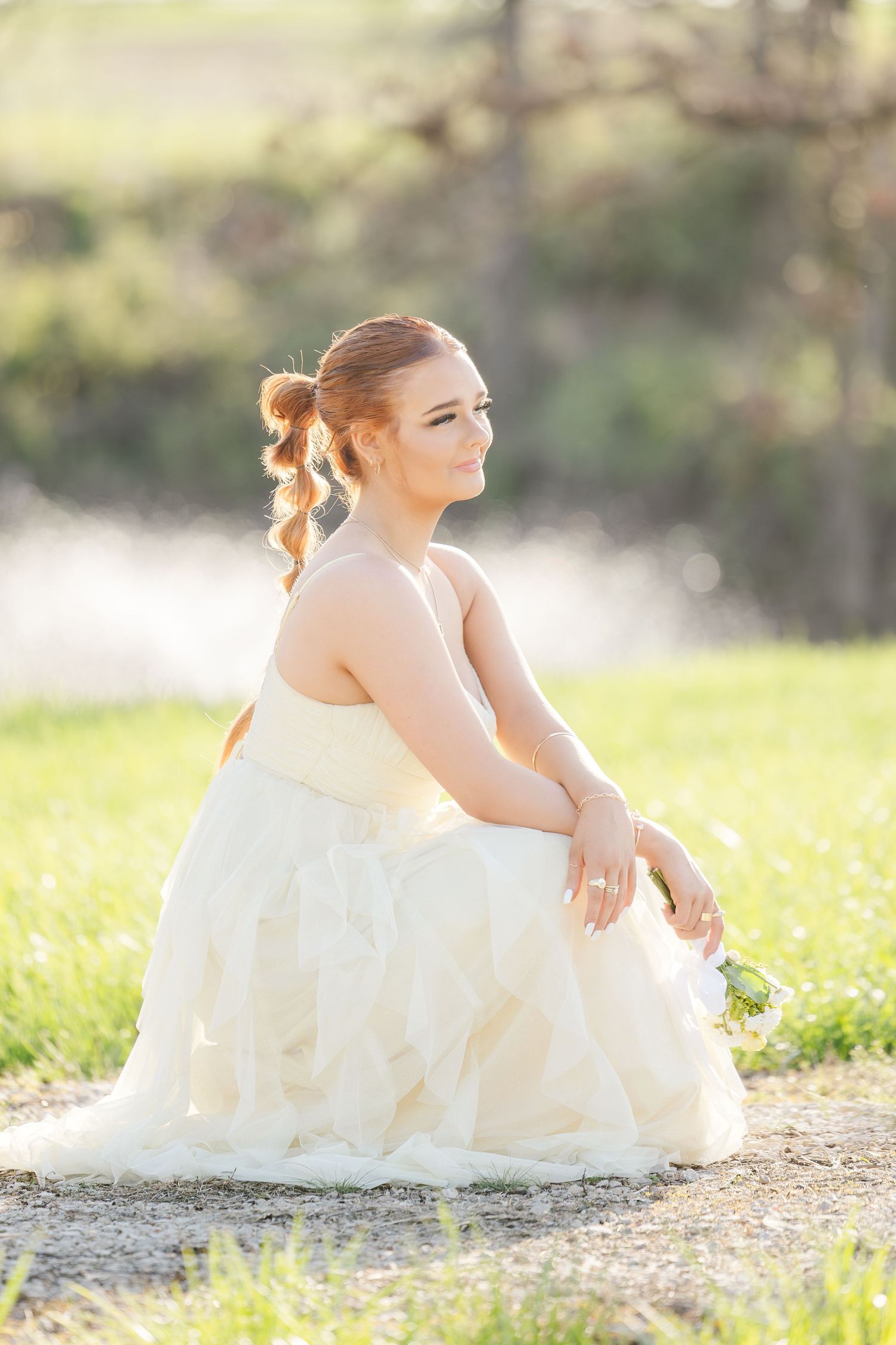 A person in an ethereal white dress sits gracefully in a sunlit meadow with a dreamy, soft-focus background.