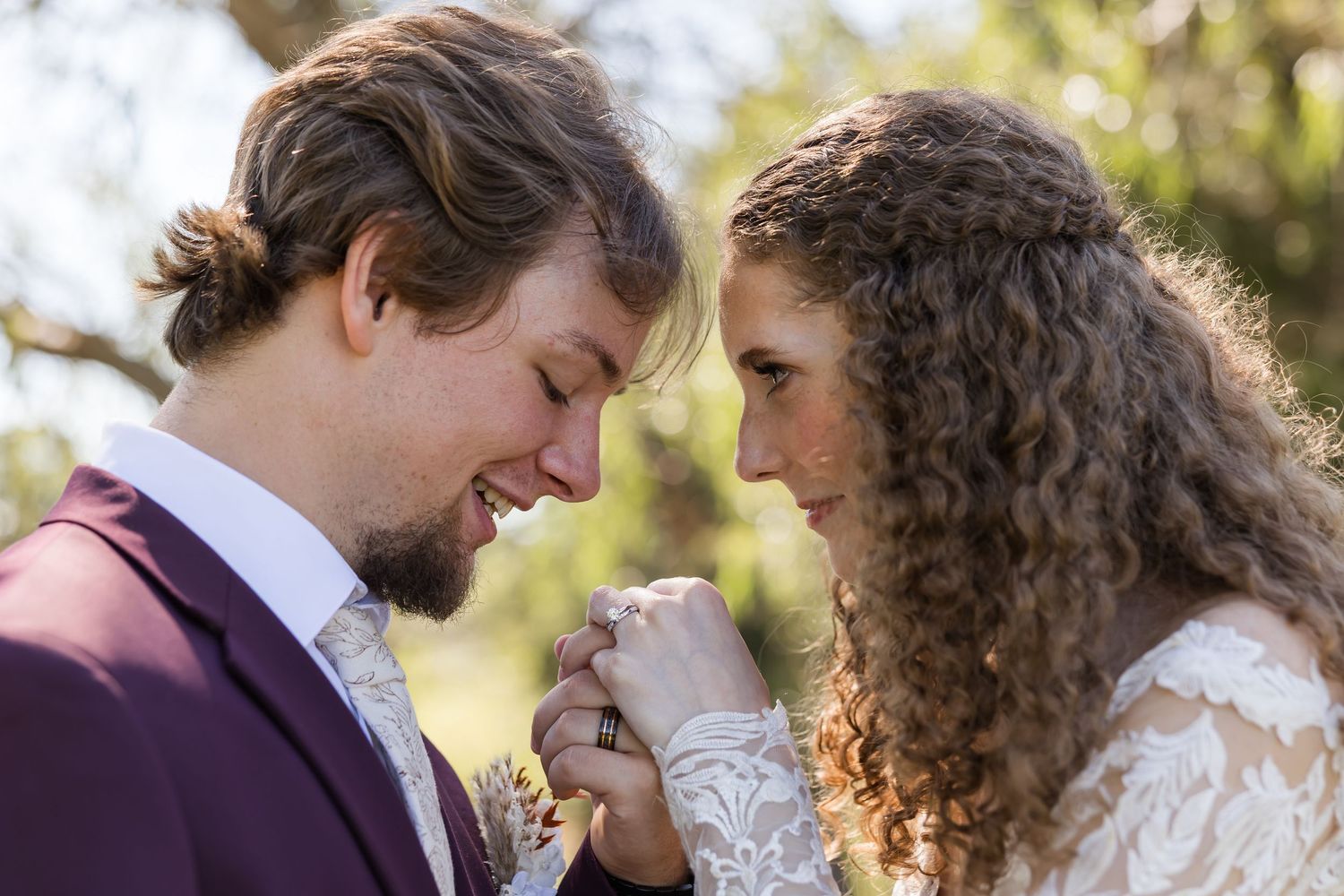 Bride and groom in intimate moment, holding hands and touching foreheads outdoors at wedding ceremony.