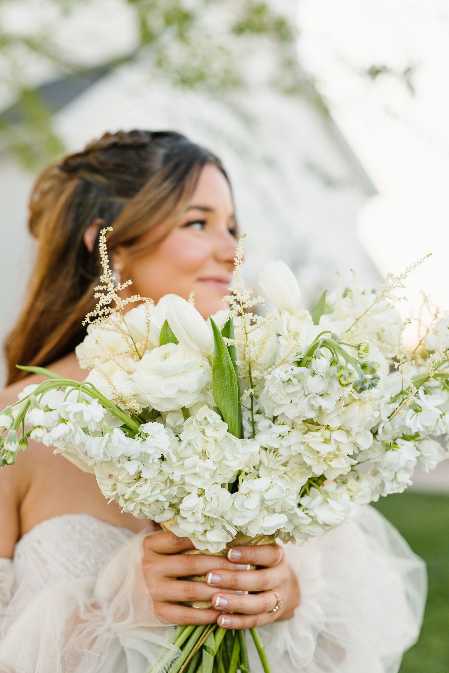 Beautiful white wedding bouquet with delicate hydrangeas and roses against a soft, natural outdoor background.