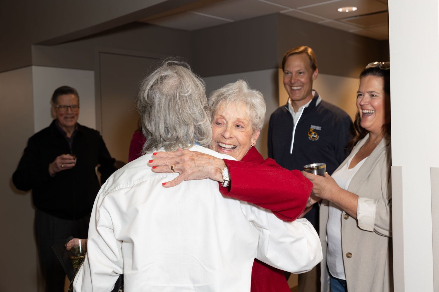 People sharing warm embrace at social gathering in office hallway.