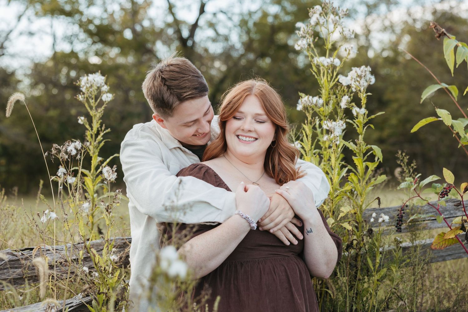 Couple shares an intimate moment among wild grasses and flowering plants in afternoon light.