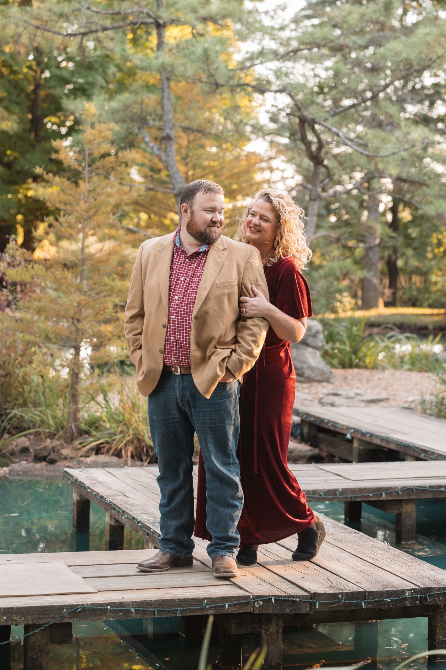A couple stands together on a wooden dock surrounded by fall colors.