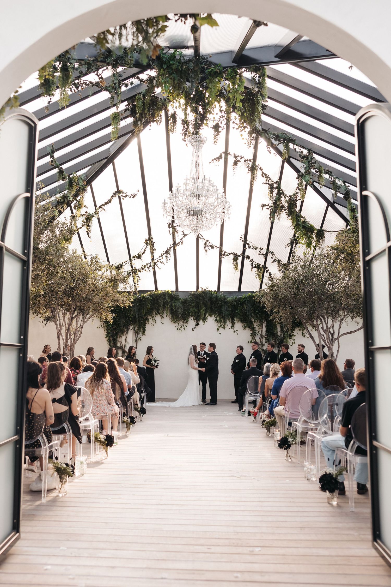 Indoor wedding ceremony venue with glass ceiling, chandelier and greenery decorations.