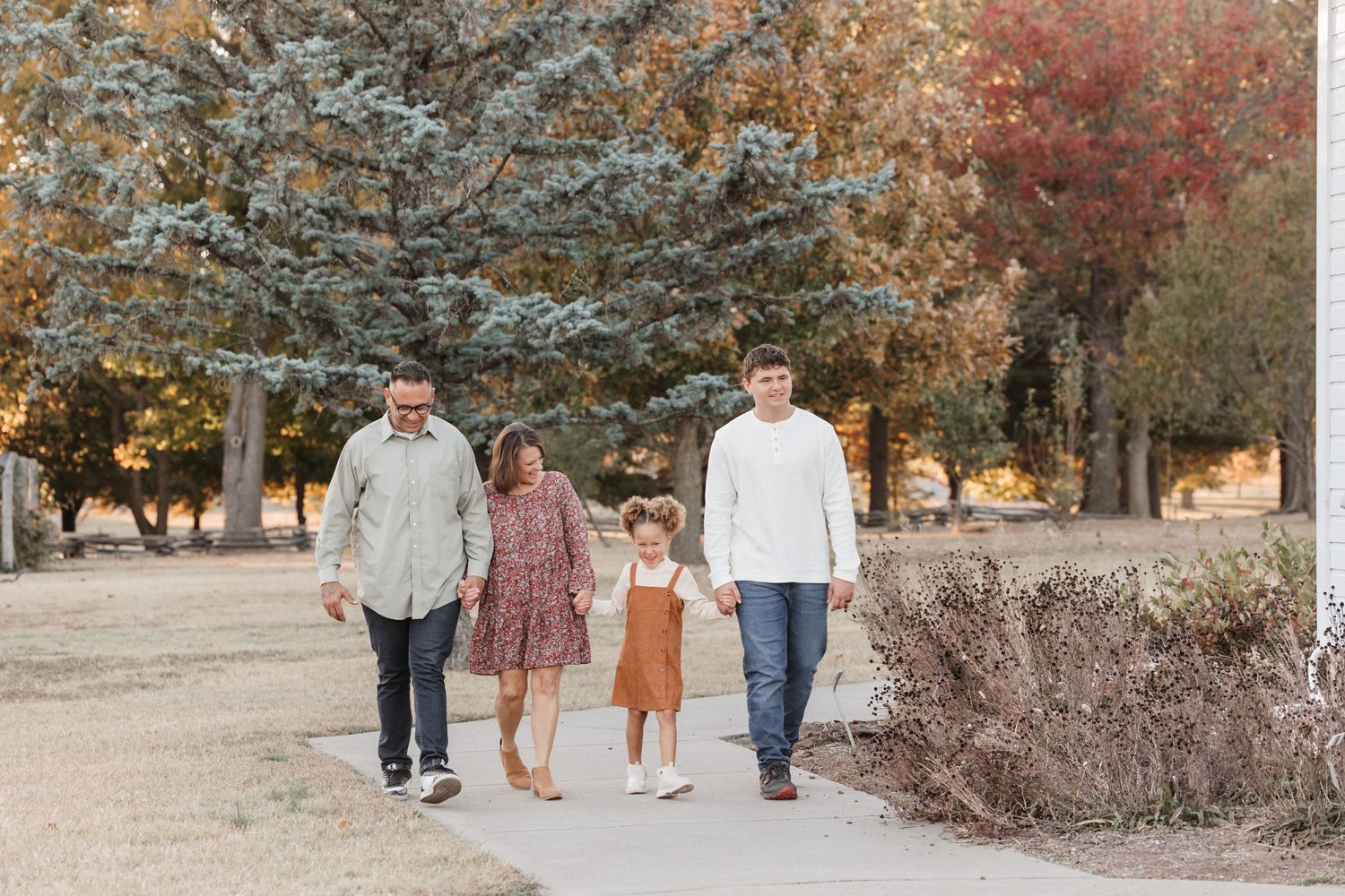 A family of four takes a casual stroll together on a path surrounded by autumn trees.