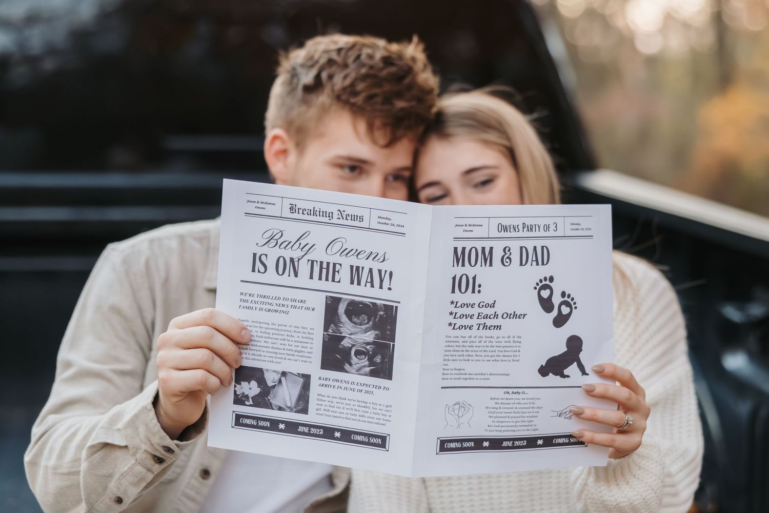 A couple holds up newspaper-style pregnancy announcement photos together in a romantic outdoor setting.