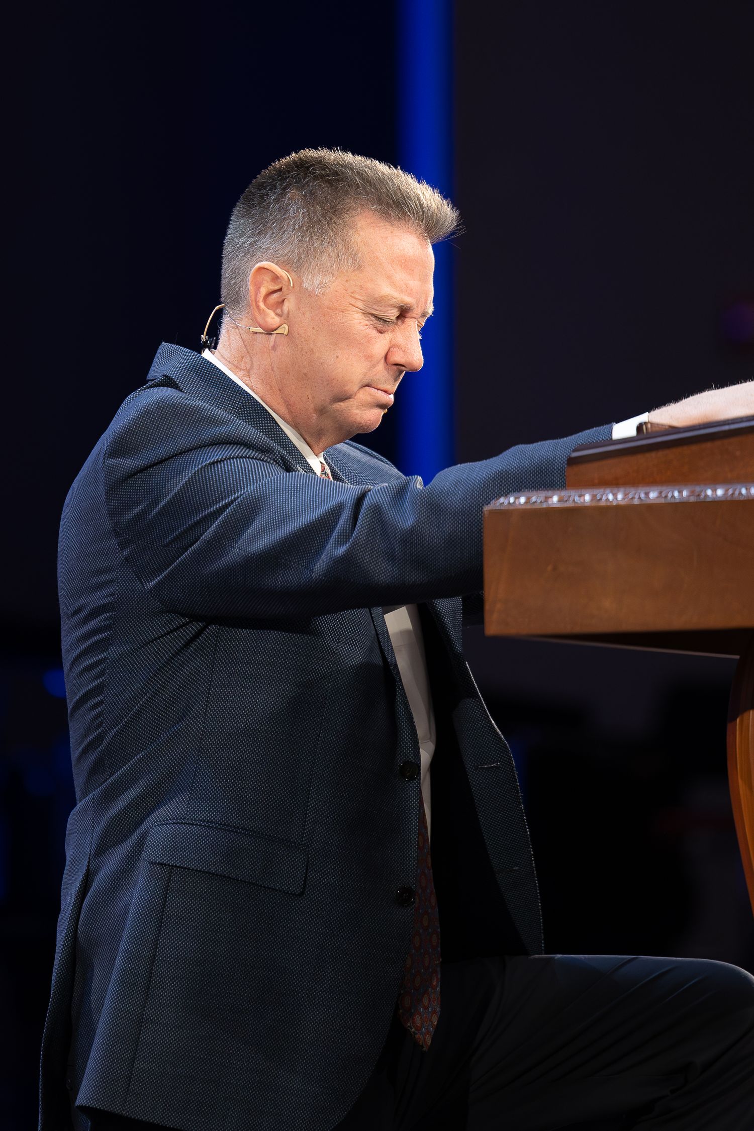 A pianist in a navy suit performs on a grand piano with dramatic lighting.