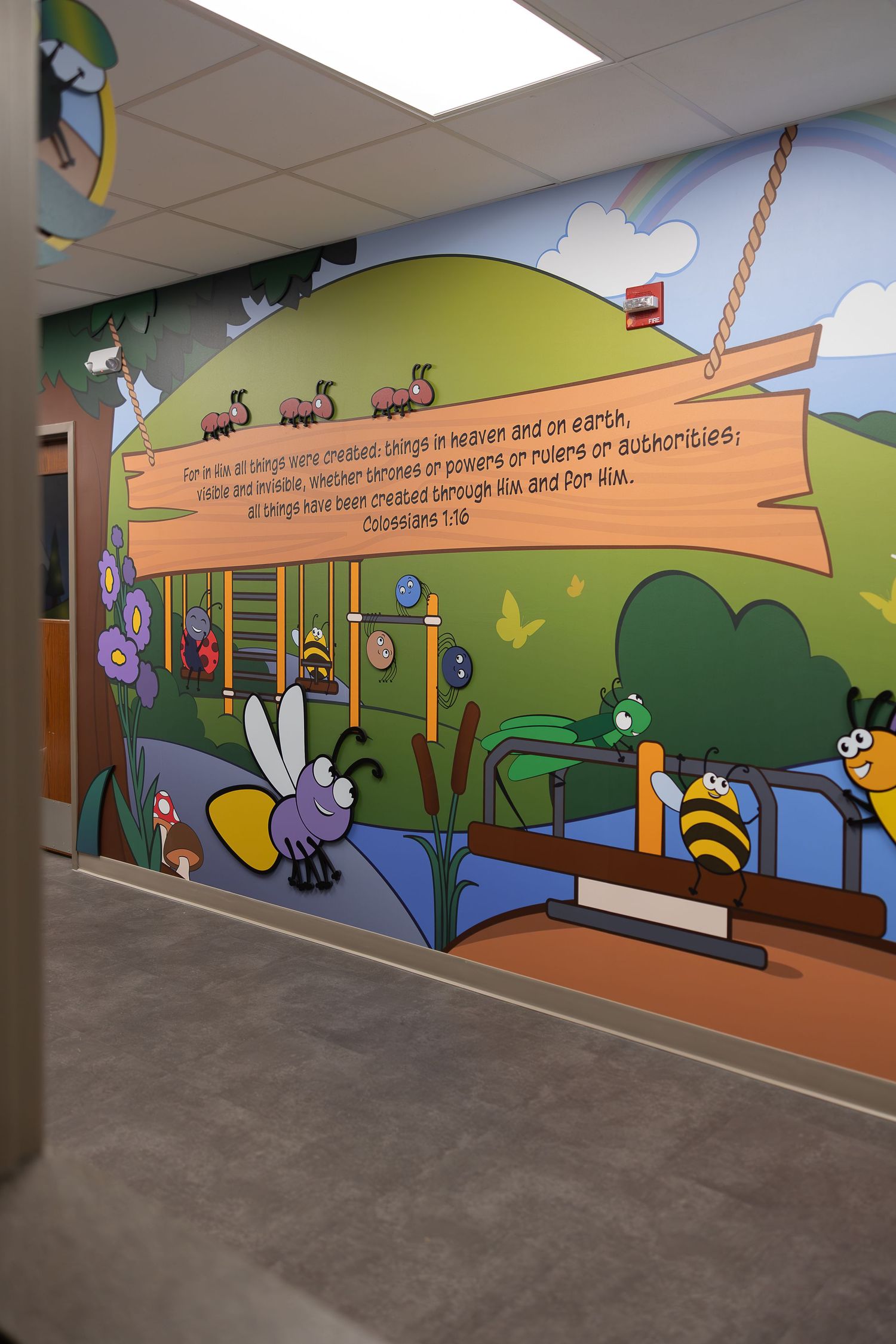 Colorful wall mural featuring cartoon insects and a wooden sign with scripture text.