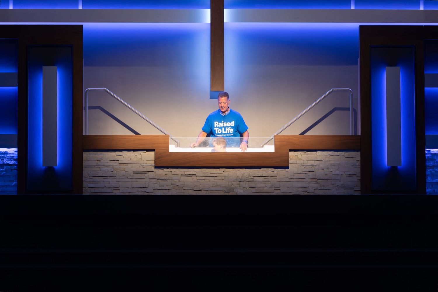 Person stands at illuminated podium on stage with blue lighting effects.