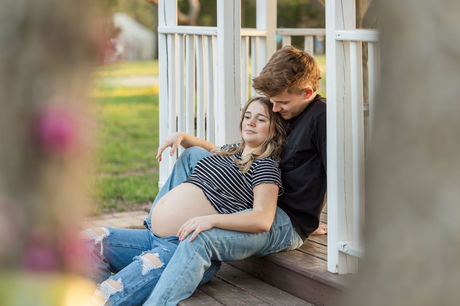A tender moment between expectant parents on a white porch during golden hour.