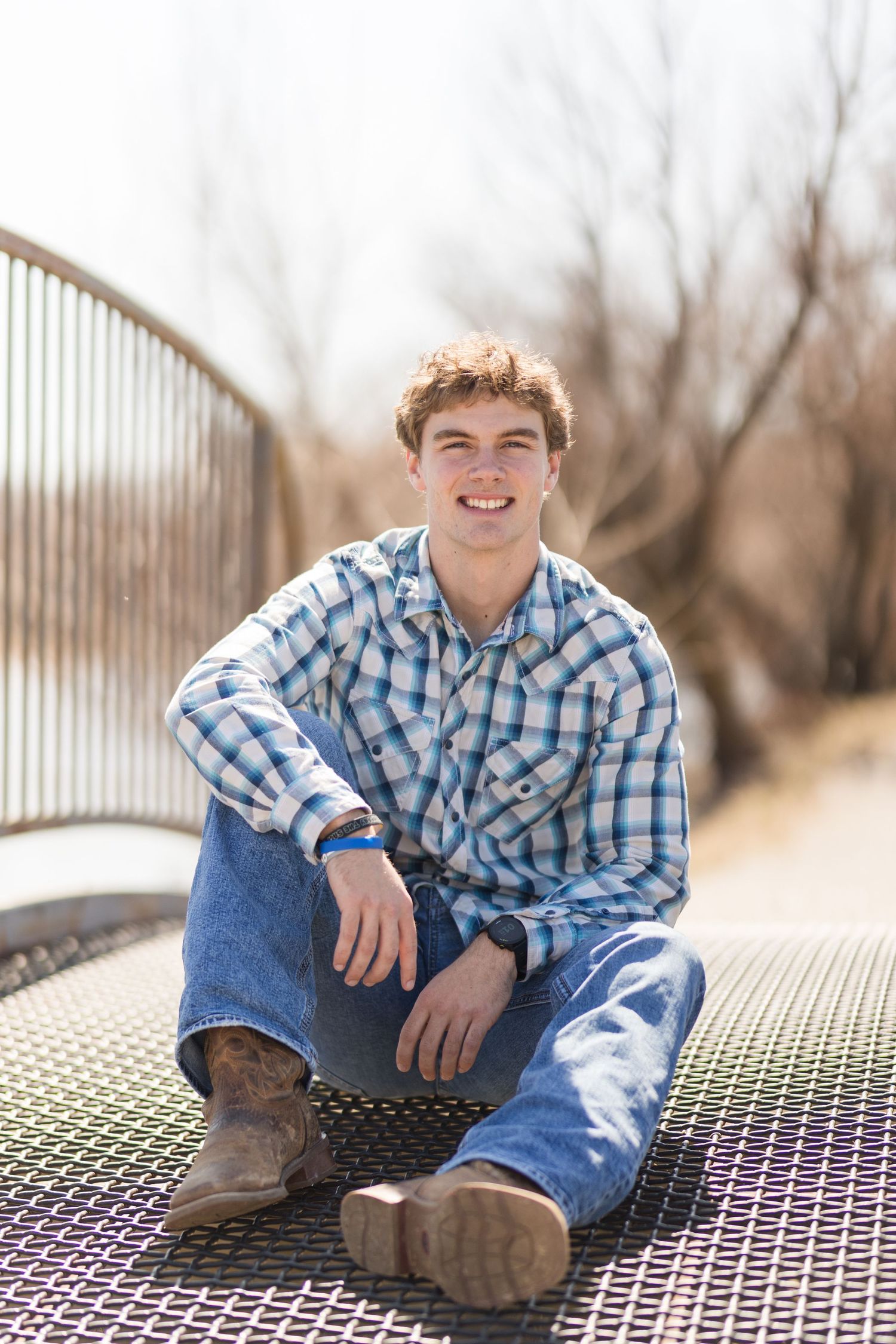 Person sitting cross-legged on metal platform wearing plaid shirt and jeans.