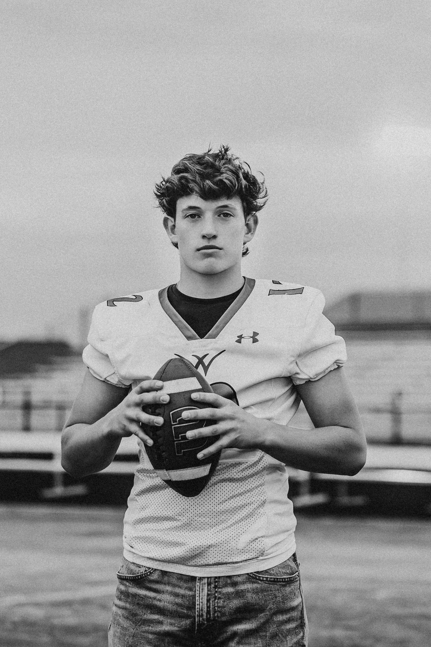 Football player poses in white uniform holding ball against stadium backdrop.