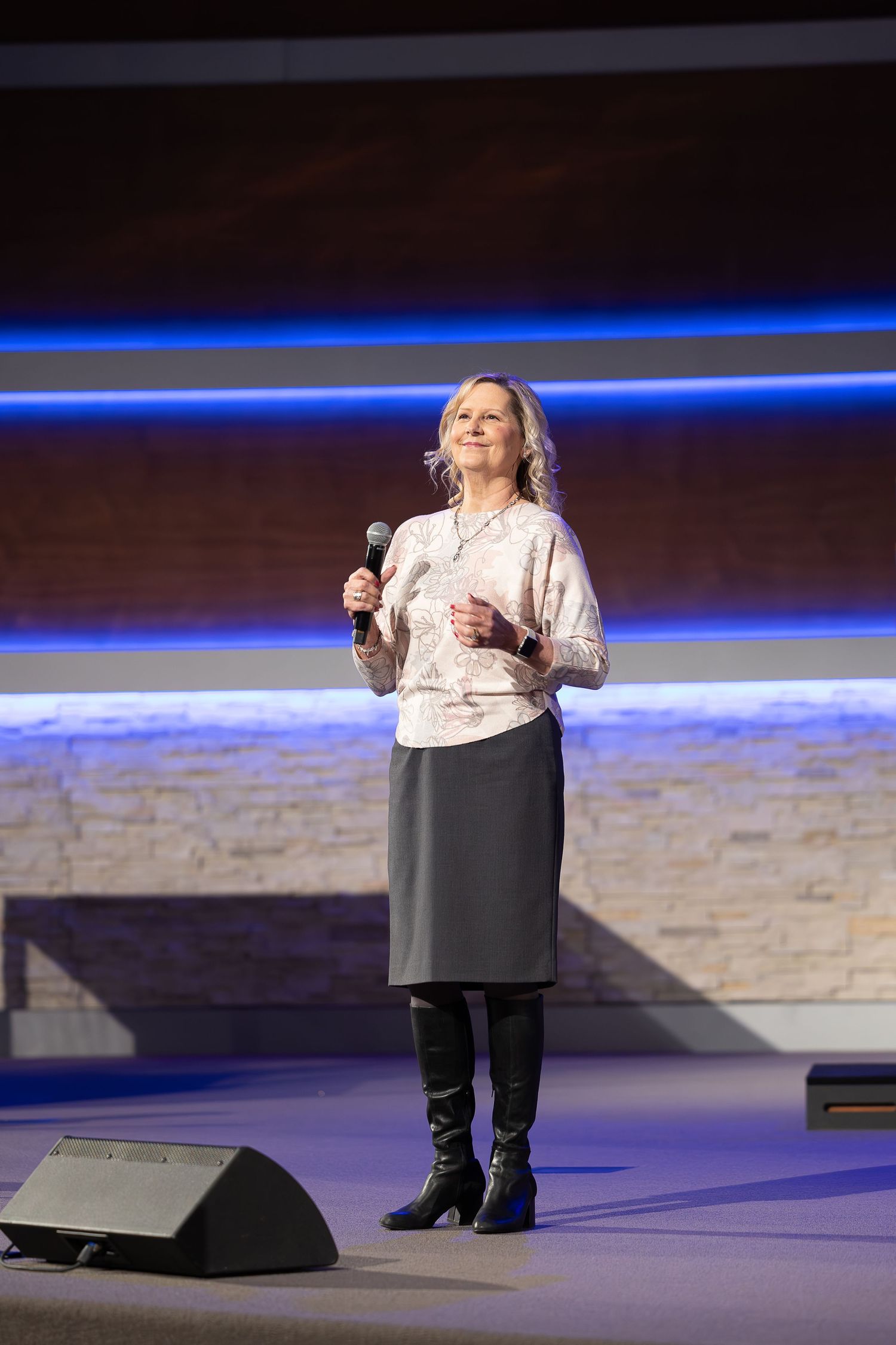 A performer in boots and skirt speaking into a microphone on stage.