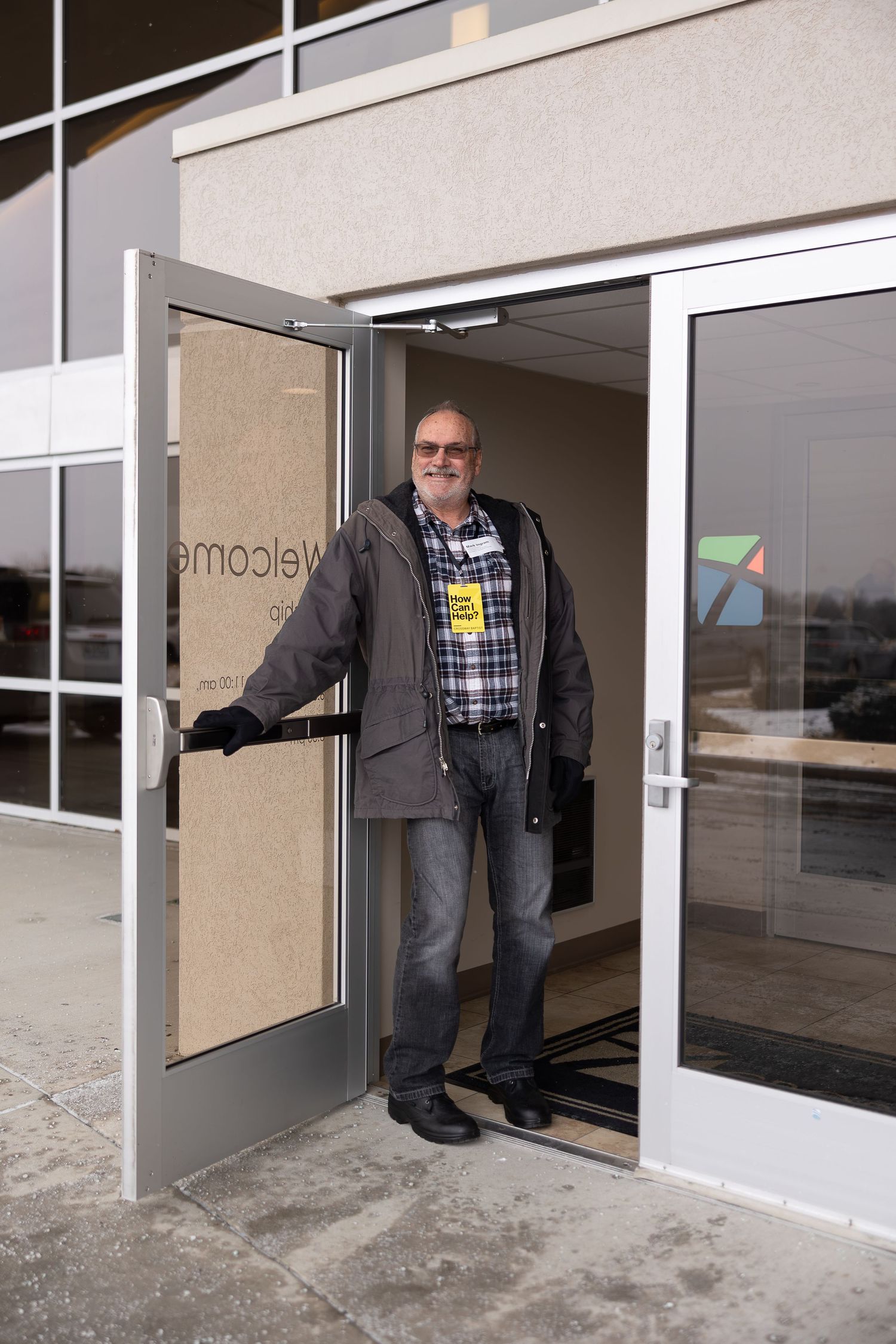 Person holding open glass entrance door at modern building entrance.