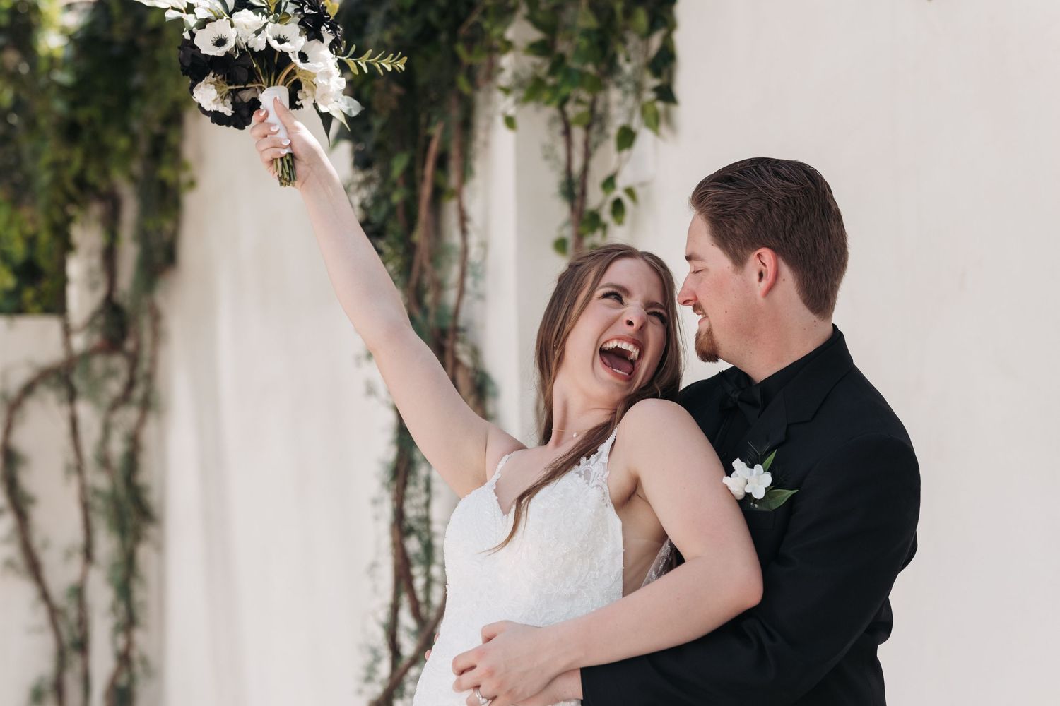 A joyful couple shares a candid moment during their wedding celebration surrounded by greenery and white decor.