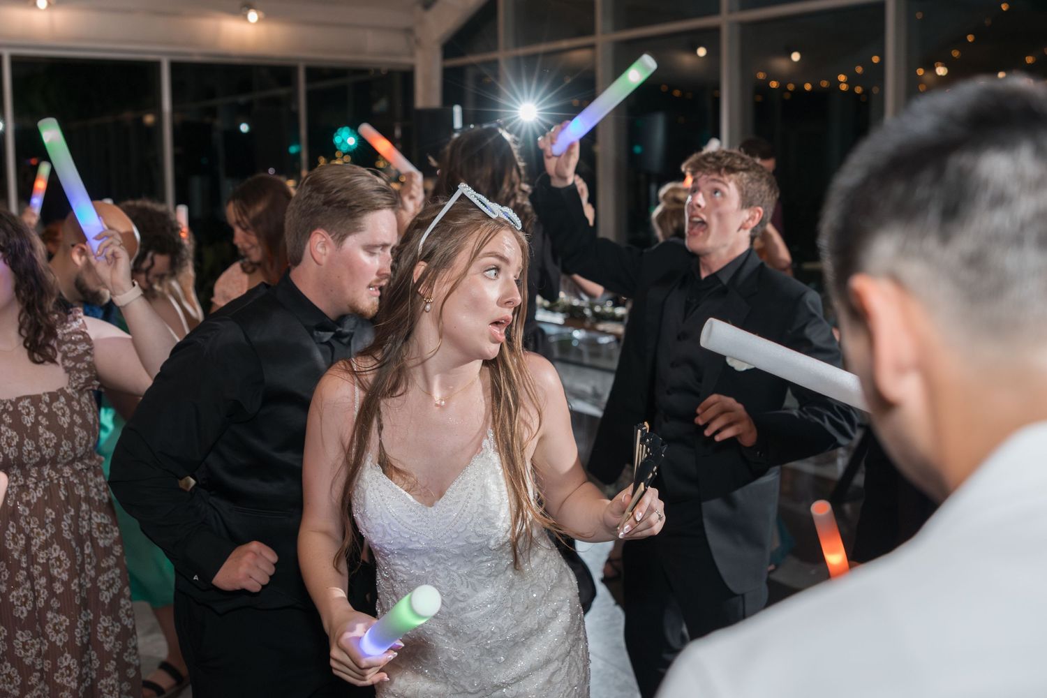 Wedding guests dance with glow sticks at an evening reception.