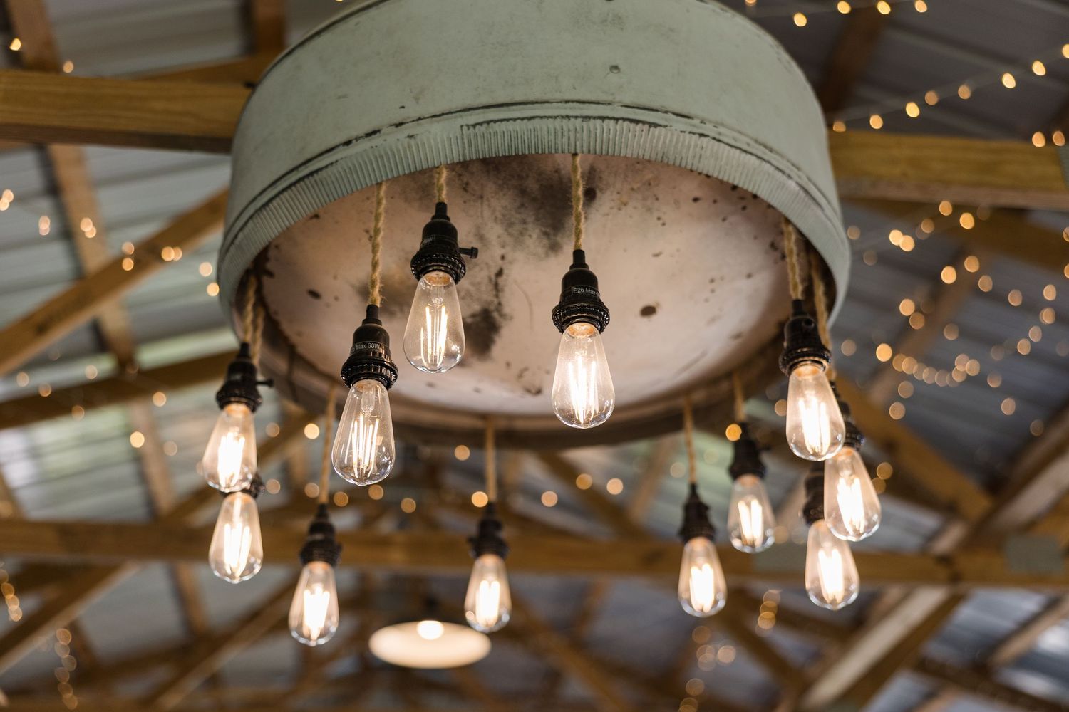 Rustic industrial light fixture with Edison bulbs hanging from a metal drum shade against a twinkle-lit ceiling.