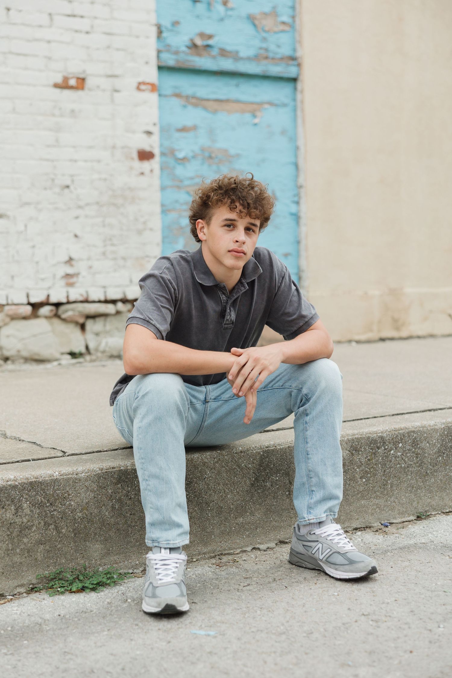 A casual street portrait with light-wash jeans and sneakers sitting against pale blue and white painted wall.