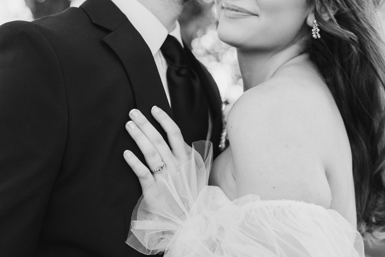Black and white wedding photo of bride and groom embracing, showcasing diamond engagement ring and elegant bridal gown.