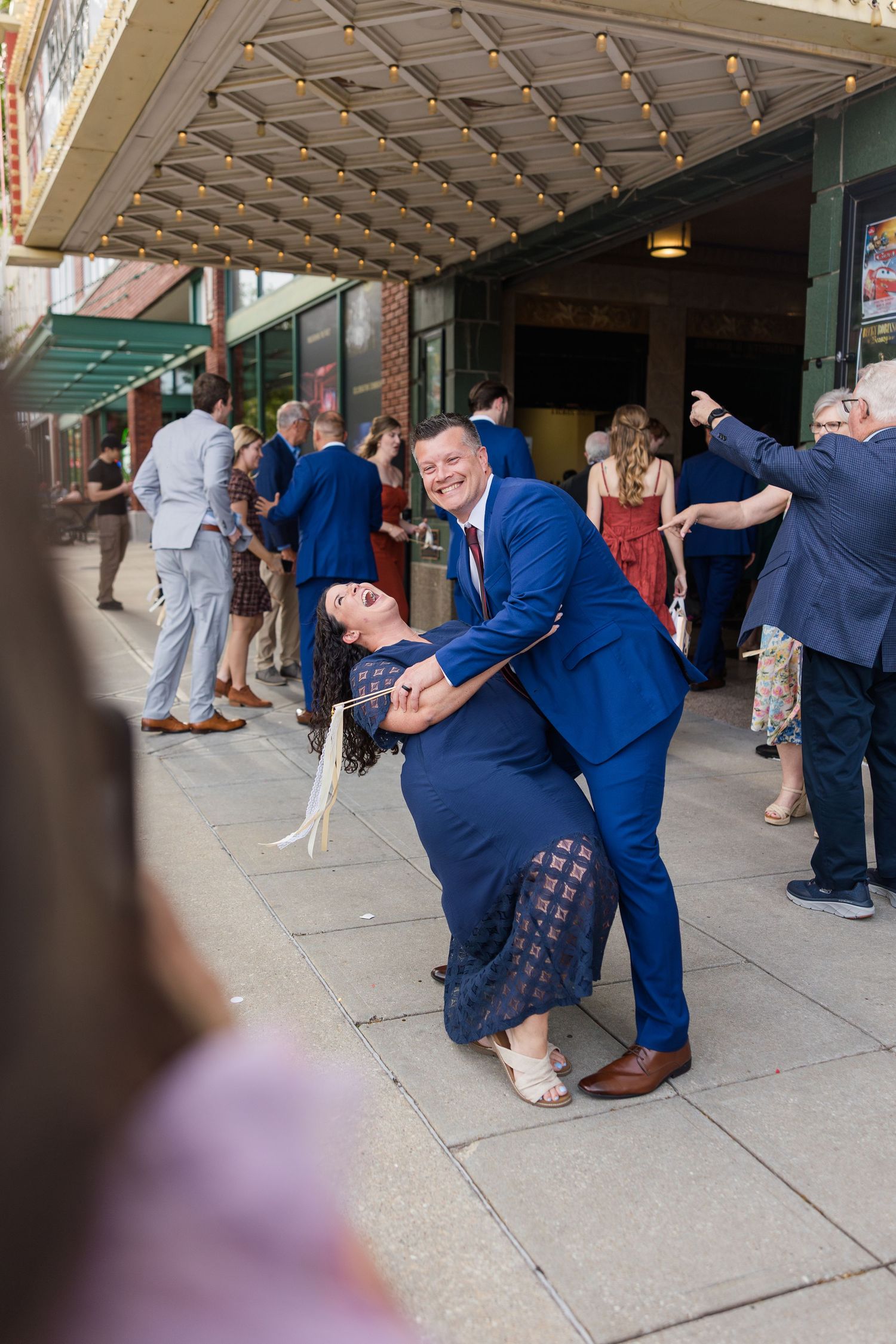 Couple dancing and dipping joyfully outside a theater venue during a wedding reception celebration.