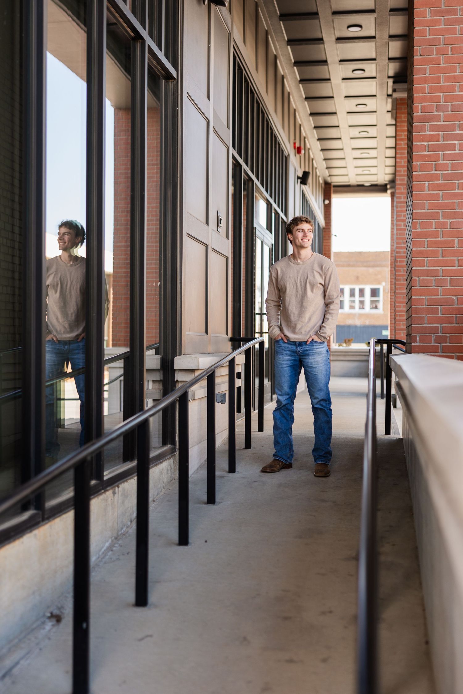 A figure stands in a modern building hallway with brick walls and large windows, creating reflective shadows.