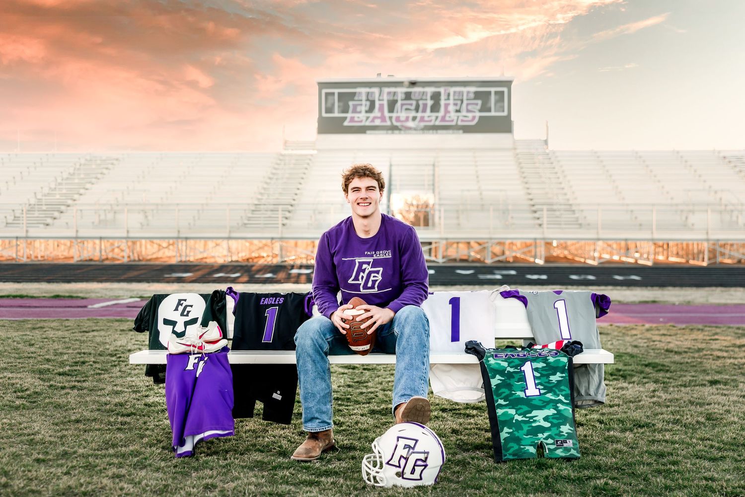 Soccer player sitting on bench with colorful sports equipment and ball on field during sunset.