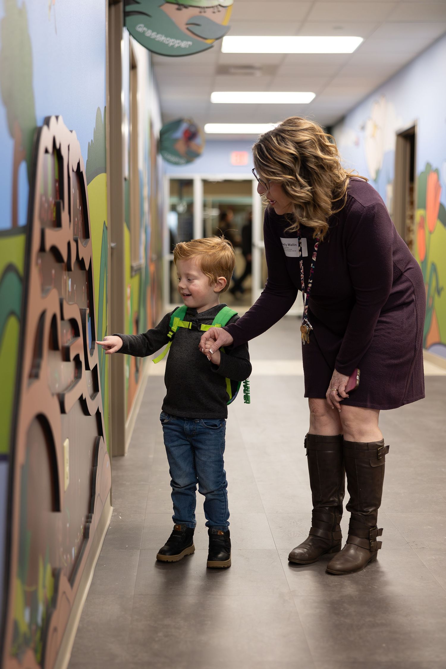 A young child touches interactive wall art in a hallway while an adult supervises.