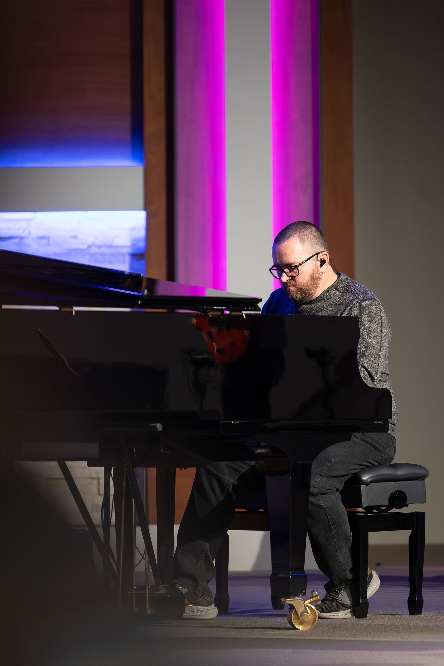 Pianist performs at grand piano on dimly lit stage with pink and blue lighting.