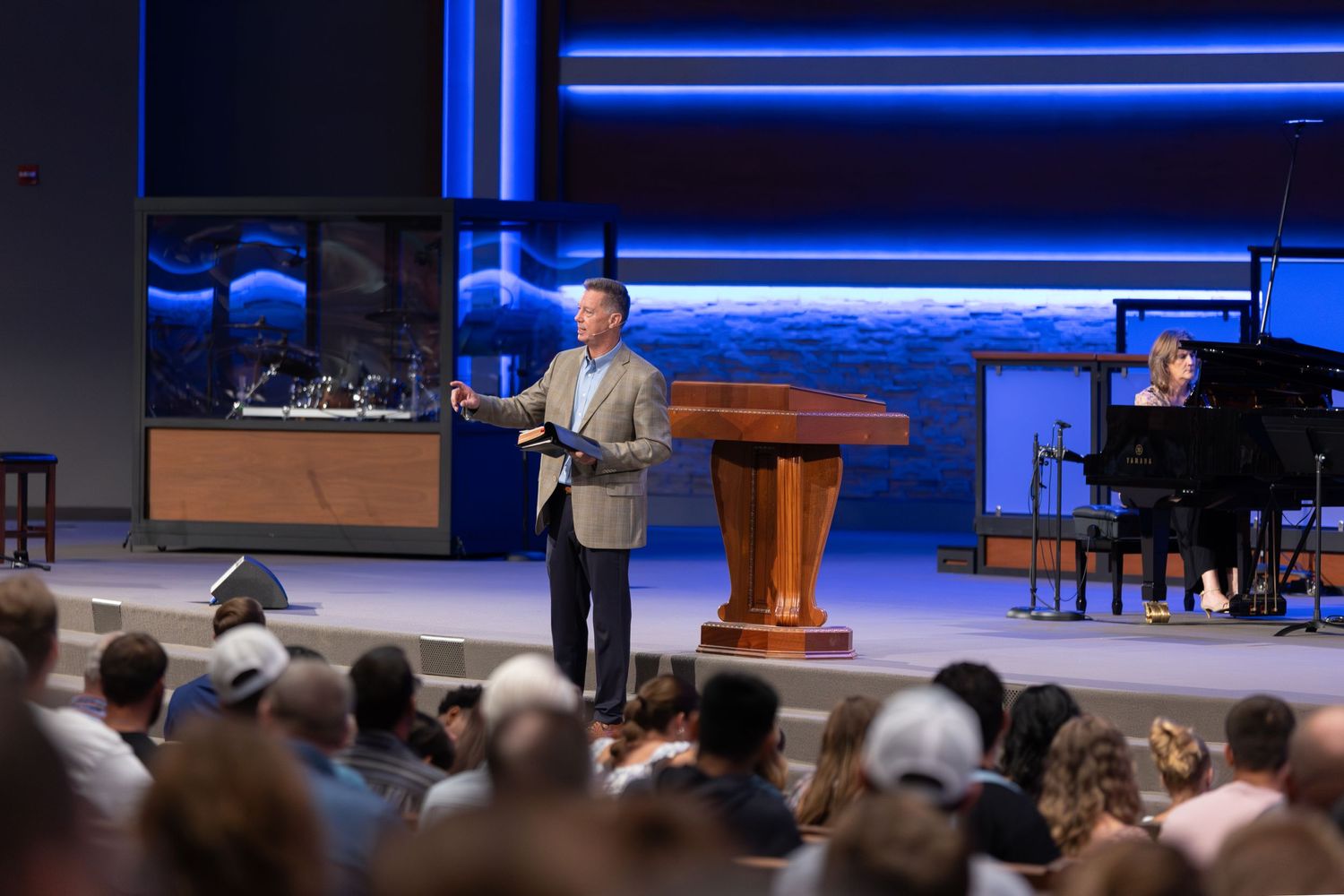A church service in progress showing a speaker on stage with projection screens and audience seating.