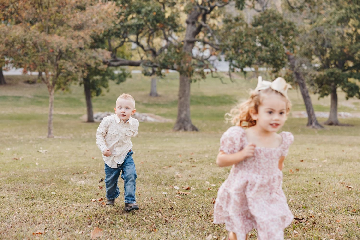 Two children run and play in a grassy field during autumn.