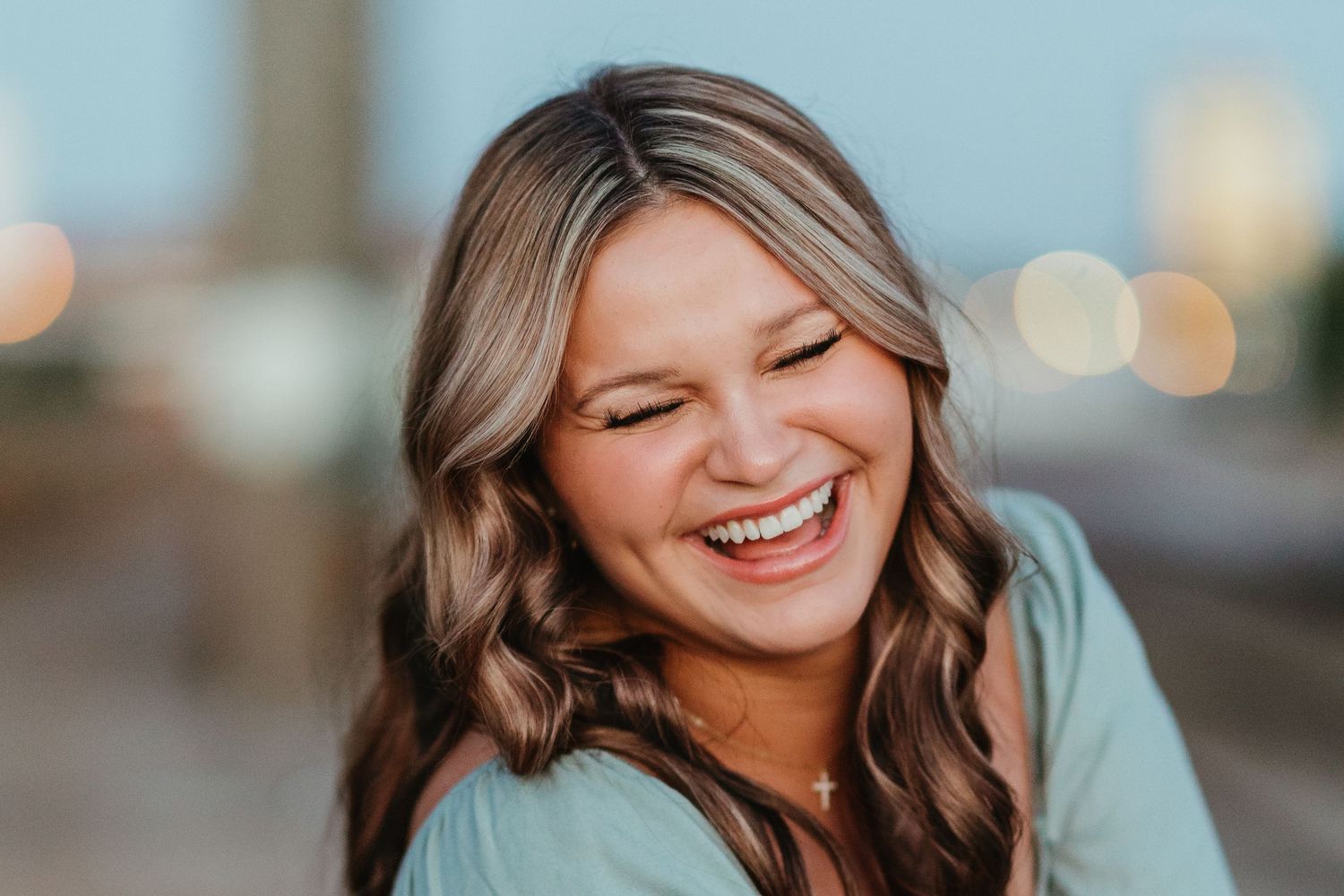Person with wavy hair laughs genuinely against blurred city lights.
