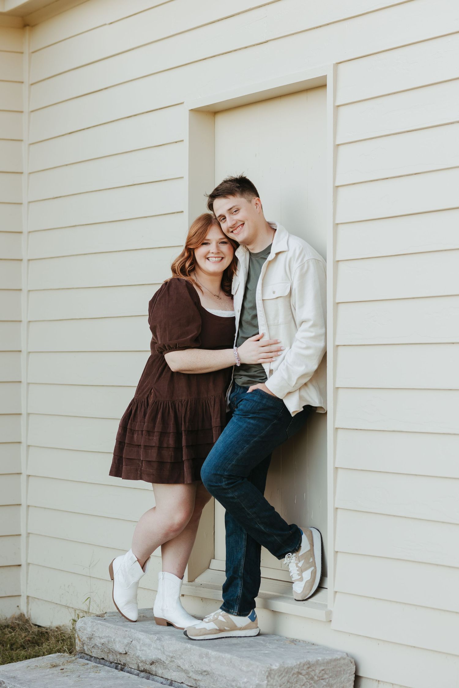 Joyful couple embracing on doorstep wearing coordinated casual outfits.