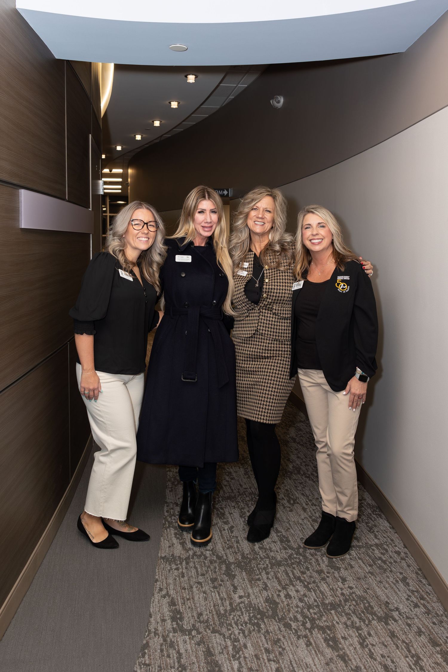 Professional women posing together in a modern office hallway wearing business casual attire.