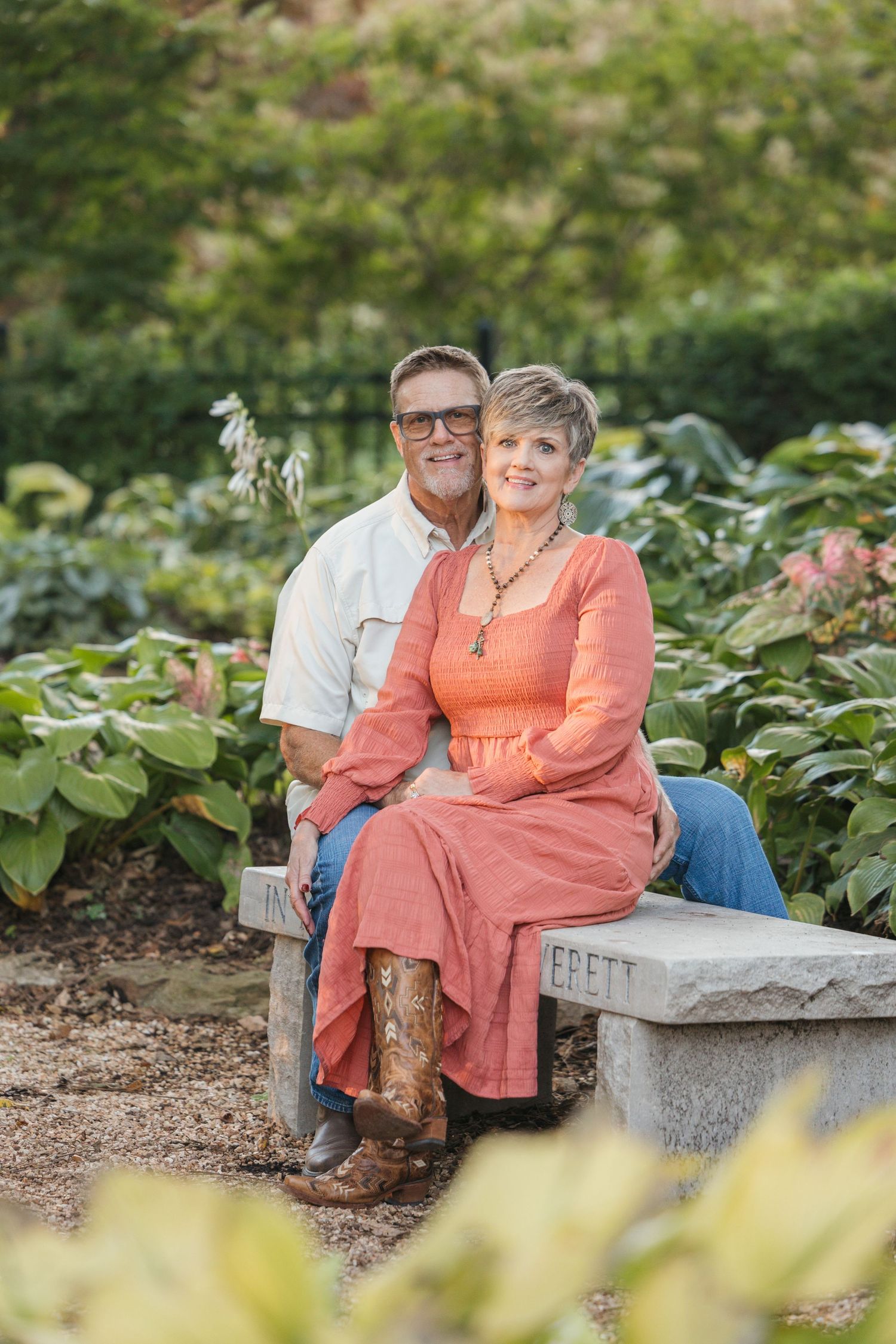 Mature couple sitting on stone bench in lush garden setting during summer.