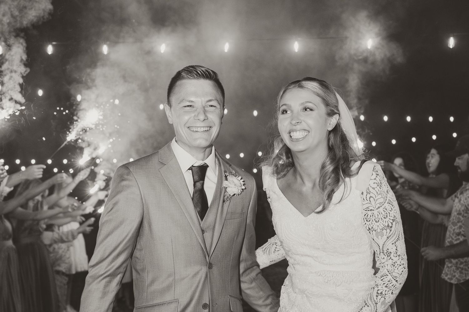 Black and white portrait of newlyweds with sparklers and string lights creating magical ambiance.