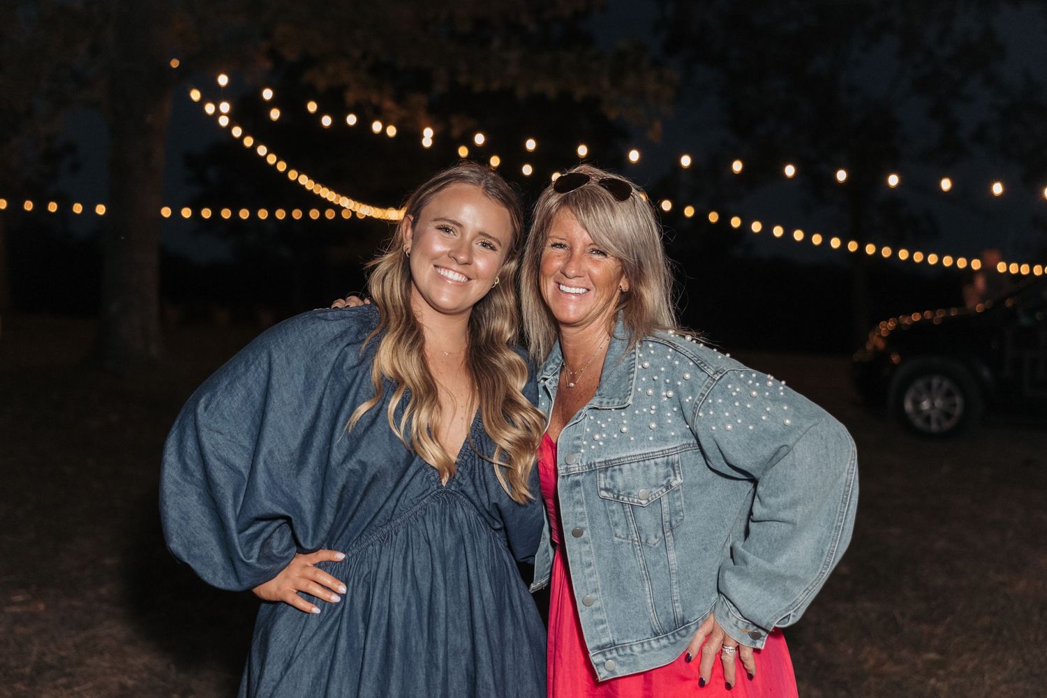 Candid nighttime portrait under glowing string lights at outdoor wedding reception.