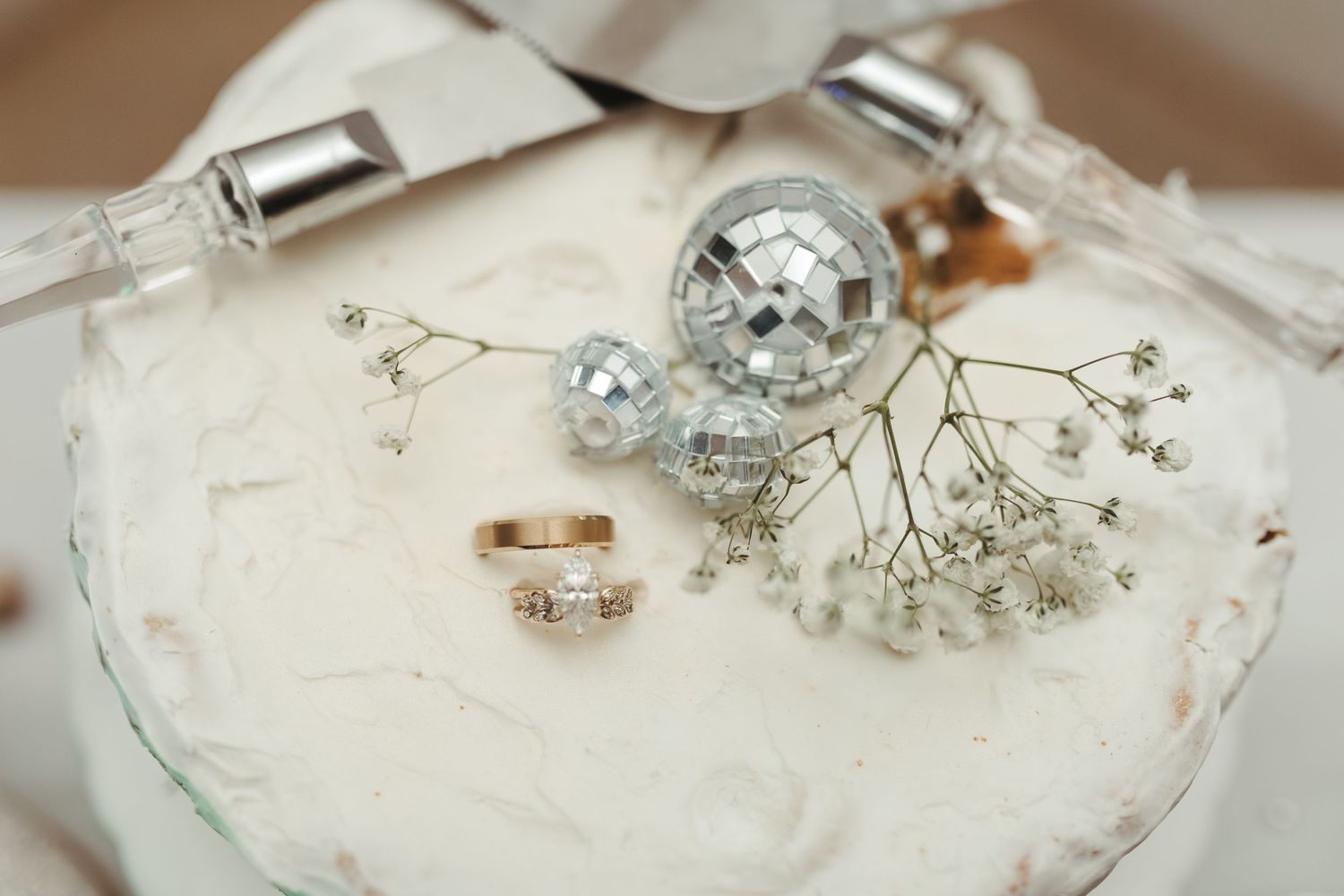 Wedding details including rings and baby's breath on a light surface with disco ball decor.