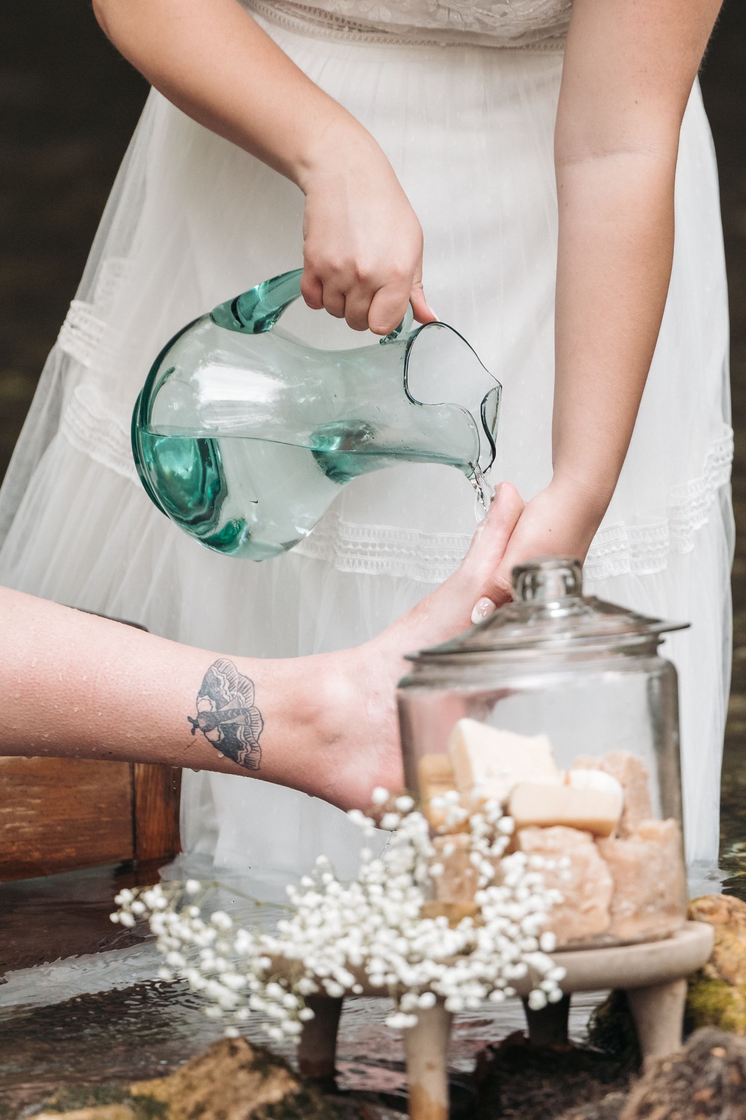Hands pour water from a teal glass pitcher into a jar decorated with baby's breath flowers.