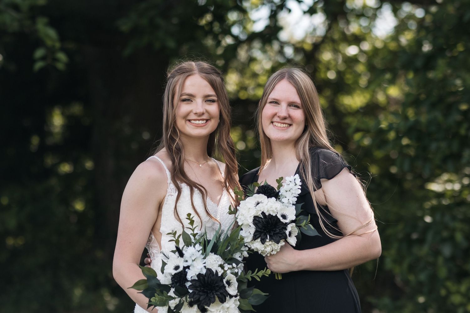 Two wedding attendants pose with matching black and white floral bouquets outdoors.
