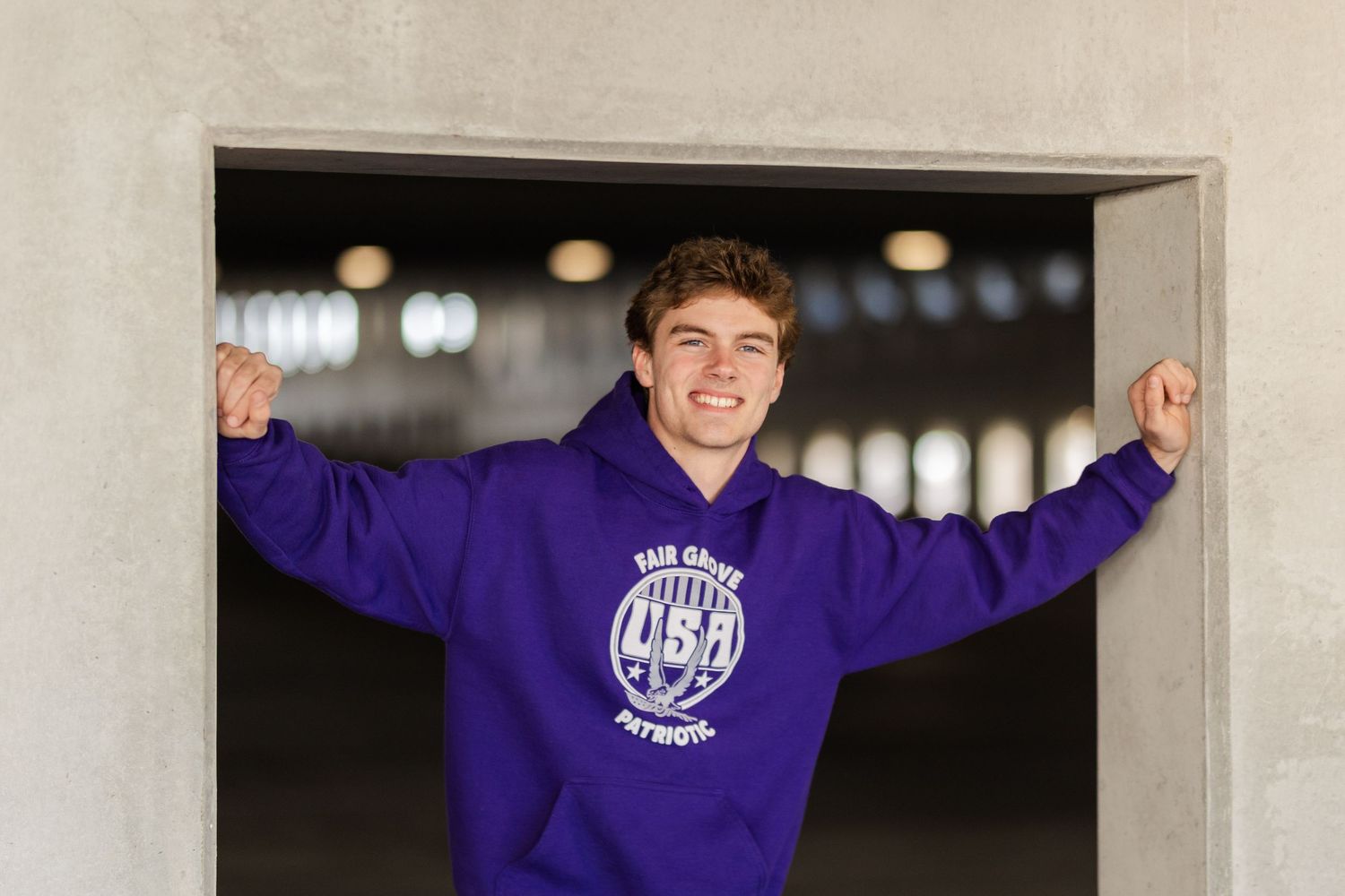 Someone wearing a purple collegiate sweatshirt poses with arms raised in a doorway.