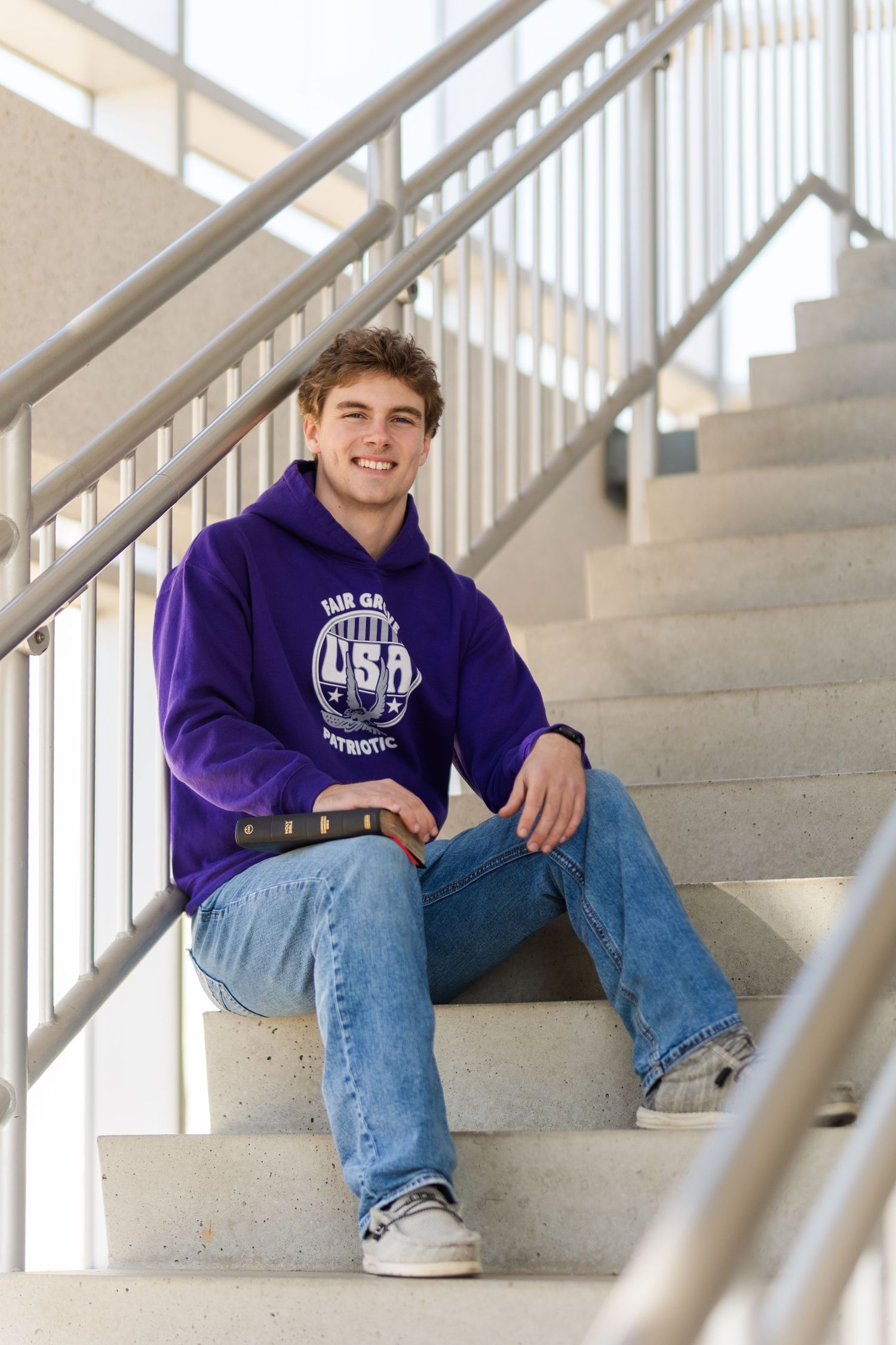 Student in purple university hoodie sitting on concrete steps with metal railing.
