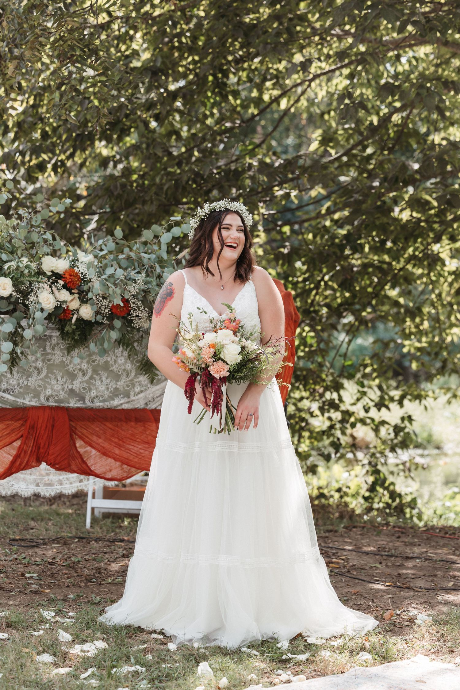 Bride in flowing white dress holds bouquet against natural outdoor backdrop.