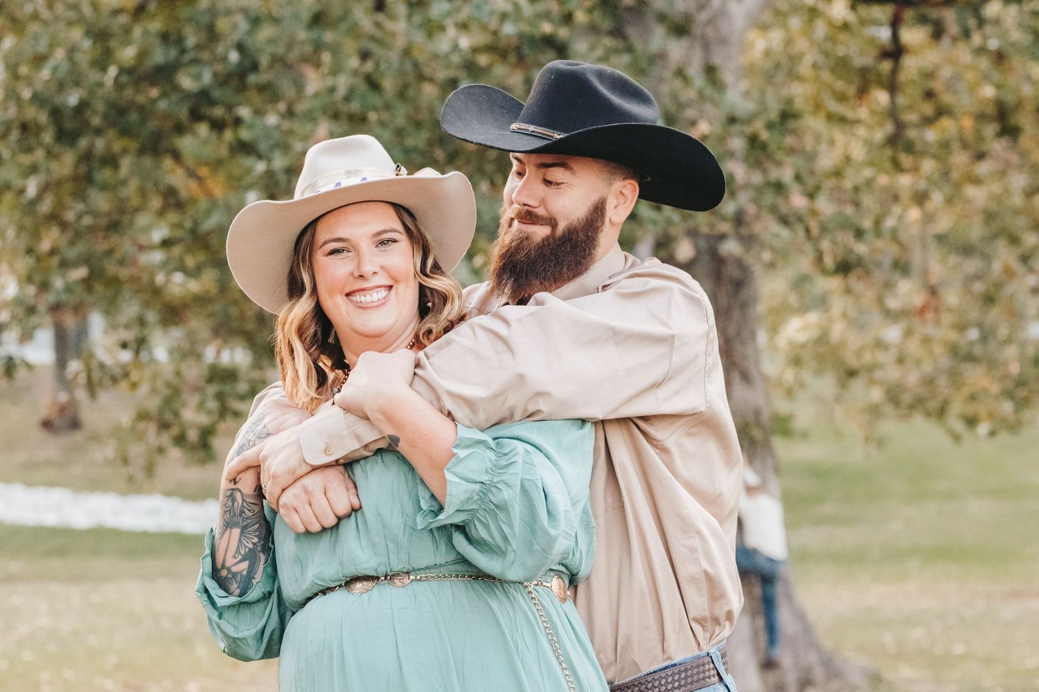 Couple in western attire embrace while sharing a romantic moment outdoors.