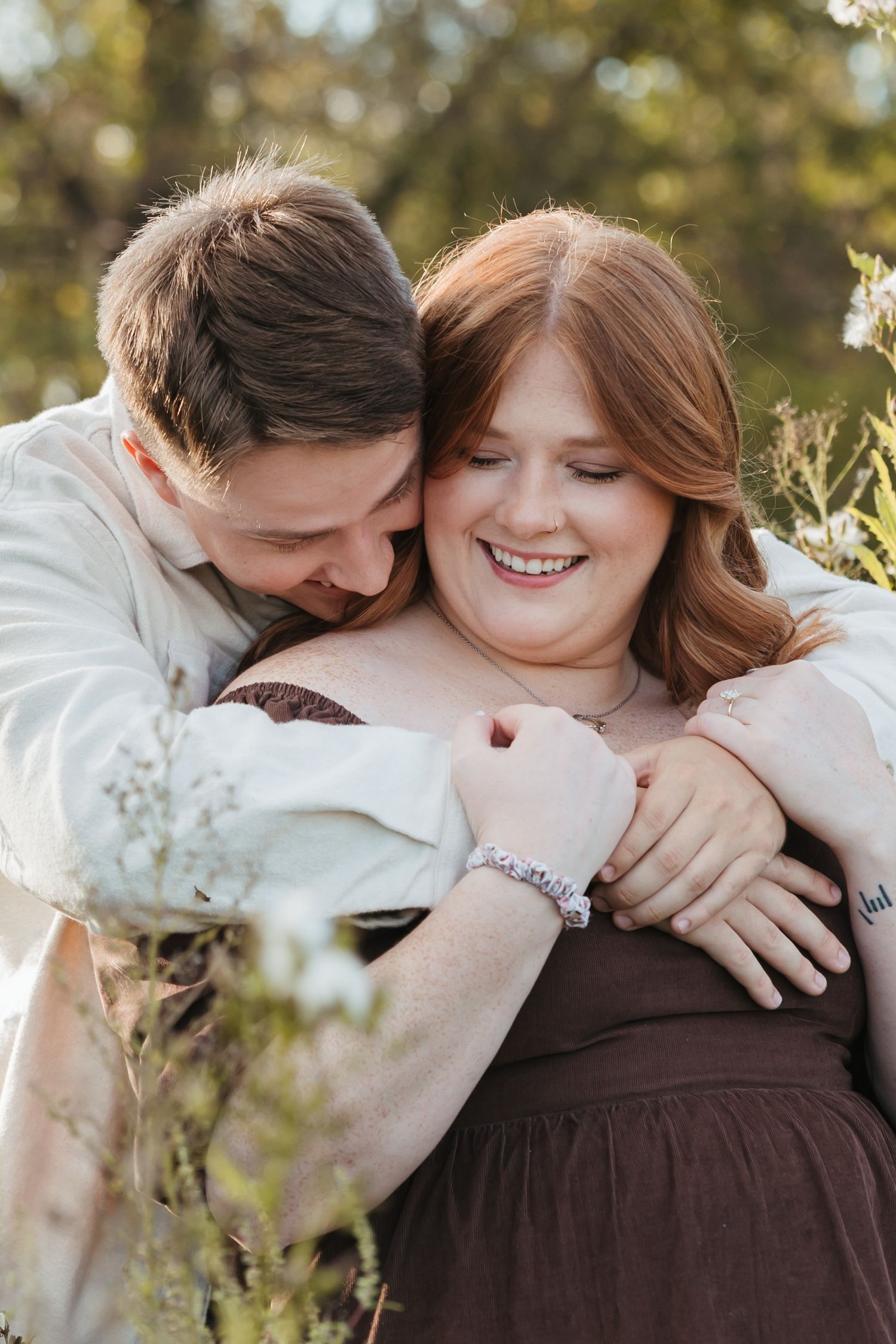 A tender moment captured between a couple sharing laughter amidst flowering plants at sunset.